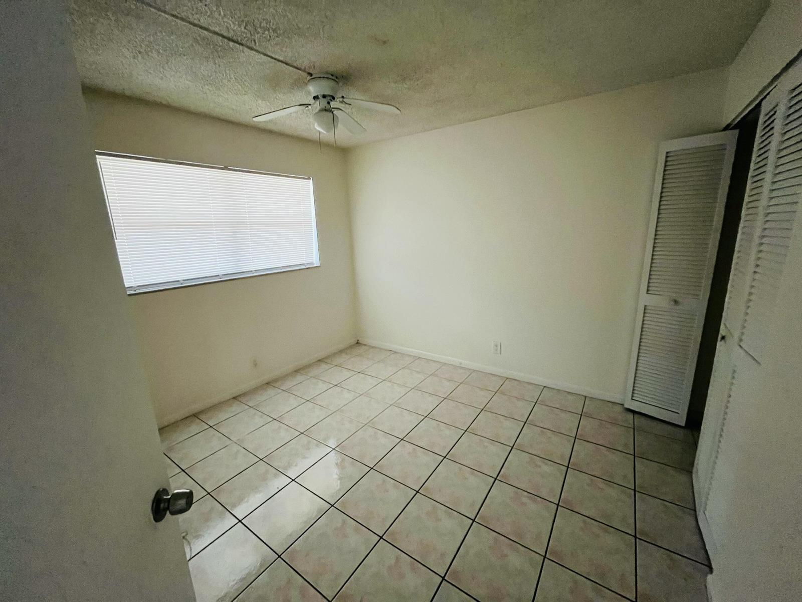 An empty bedroom features white walls, tiled flooring, a ceiling fan, and a louvered closet door — 9911 Sandalfoot Boulevard # 112, Boca Raton FL 33428, BOCA RATON, FL