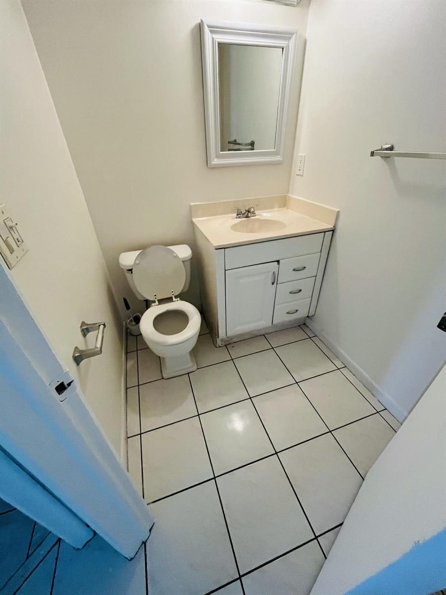 A small bathroom features a white toilet, a vanity with a sink, and tiled flooring — 9911 Sandalfoot Boulevard # 112, Boca Raton FL 33428, BOCA RATON, FL