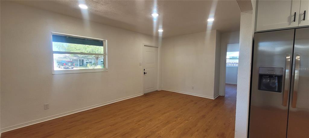 A room with wood-look flooring, a window, a door, and a stainless steel refrigerator — 6023 FLORA TERRACE, APOLLO BEACH, FL