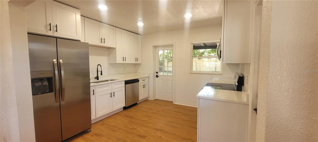 A kitchen features white cabinets, stainless steel appliances, a sink, and light wood-look flooring — 6023 FLORA TERRACE, APOLLO BEACH, FL