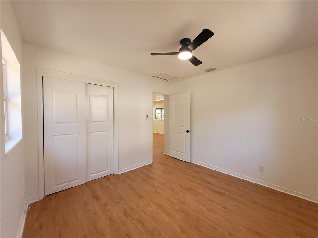 A bedroom features white walls, light wood-look flooring, a ceiling fan, and a sliding closet — 6023 FLORA TERRACE, APOLLO BEACH, FL