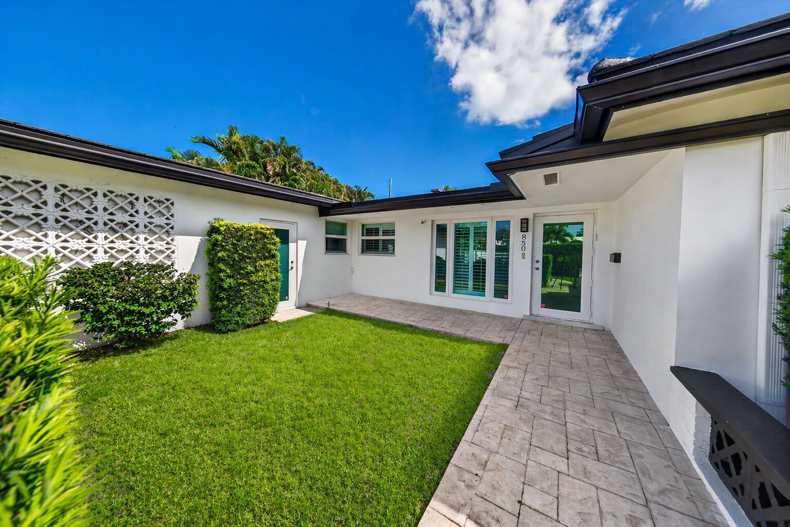 A white house exterior features a stone walkway, green lawn, and a decorative lattice wall — 850 W Camino Real, Boca Raton FL 33486, BOCA RATON, FL