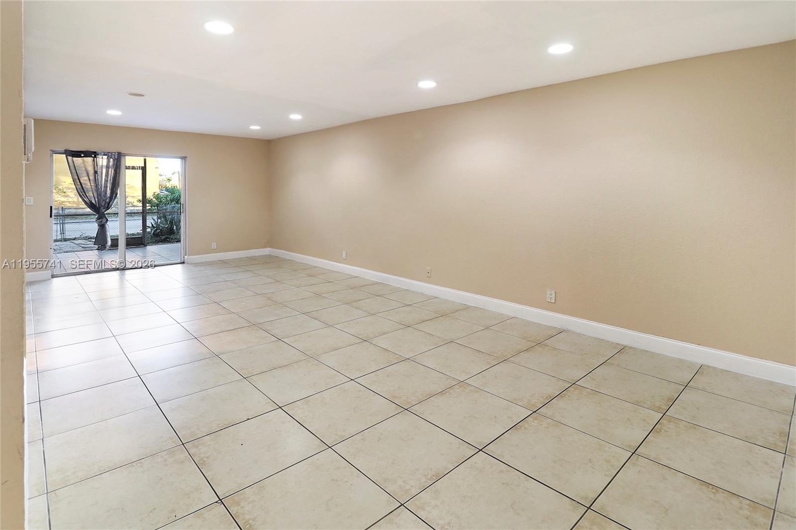 An empty room features beige walls, large square floor tiles, and a sliding glass door — 5975 NW 25th Ct # 213, Sunrise FL 33313, SUNRISE, FL