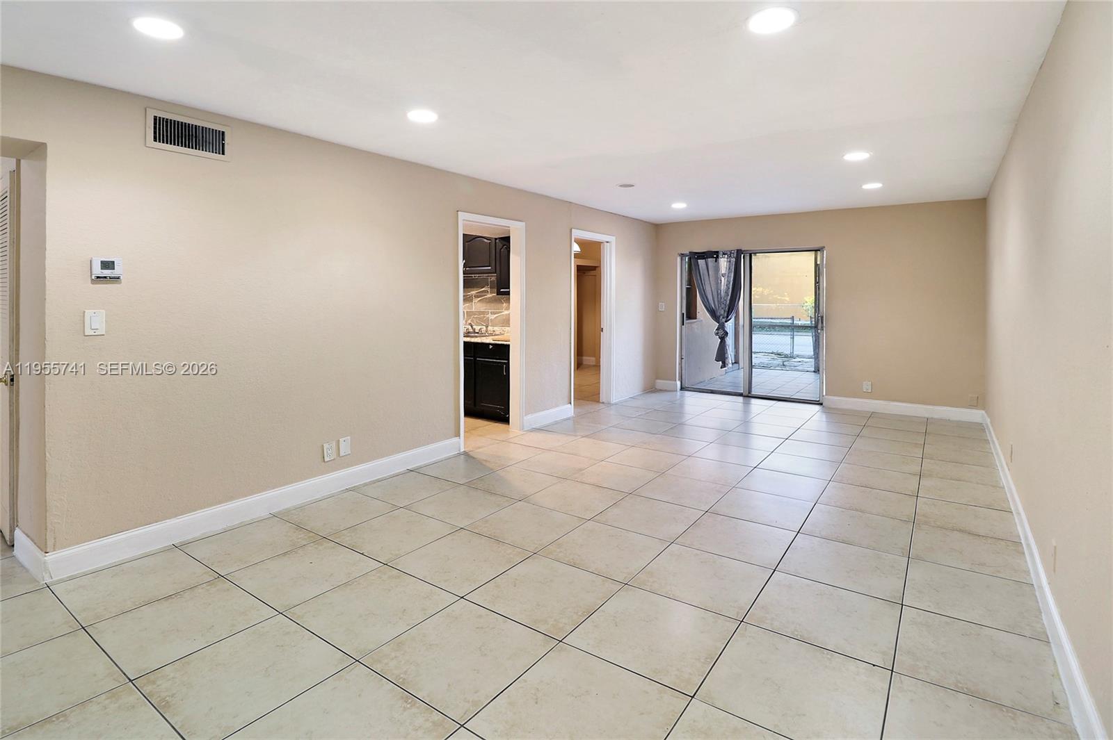 An empty living room features beige walls, light-colored tile flooring, and a sliding glass door — 5975 NW 25th Ct # 213, Sunrise FL 33313, SUNRISE, FL