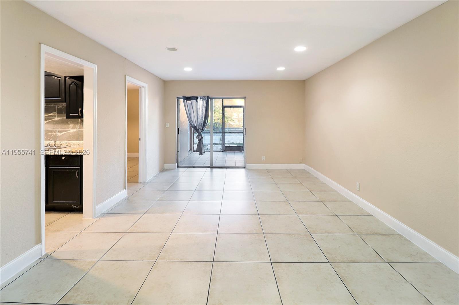 An empty room with beige walls, tile flooring, and a sliding glass door to a patio — 5975 NW 25th Ct # 213, Sunrise FL 33313, SUNRISE, FL