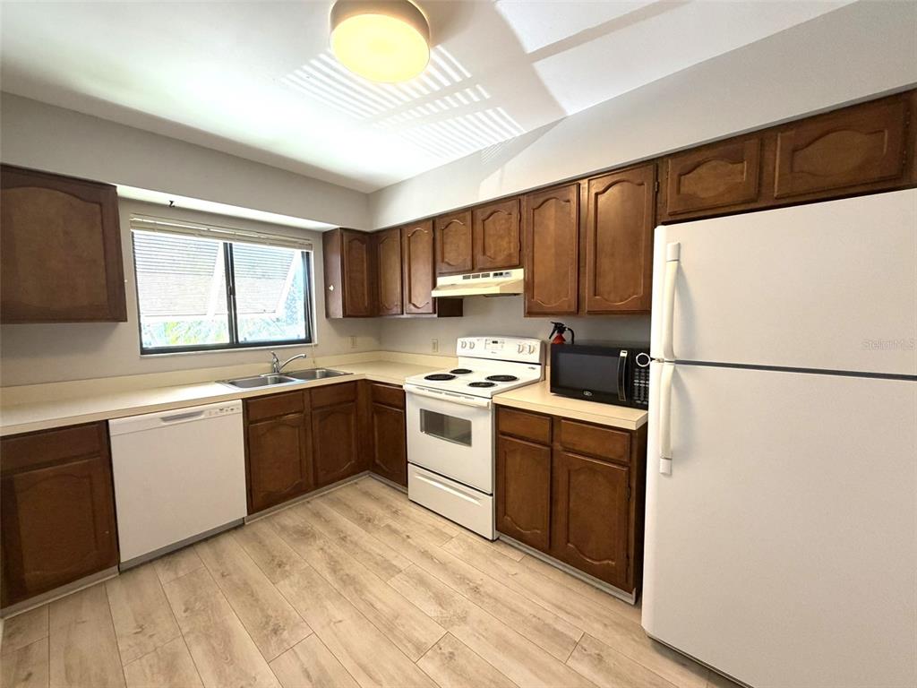 A kitchen features wood cabinets, white appliances, a double sink, and light wood-look flooring — 5216 WILLOW LINKS UNIT 82, SARASOTA, FL
