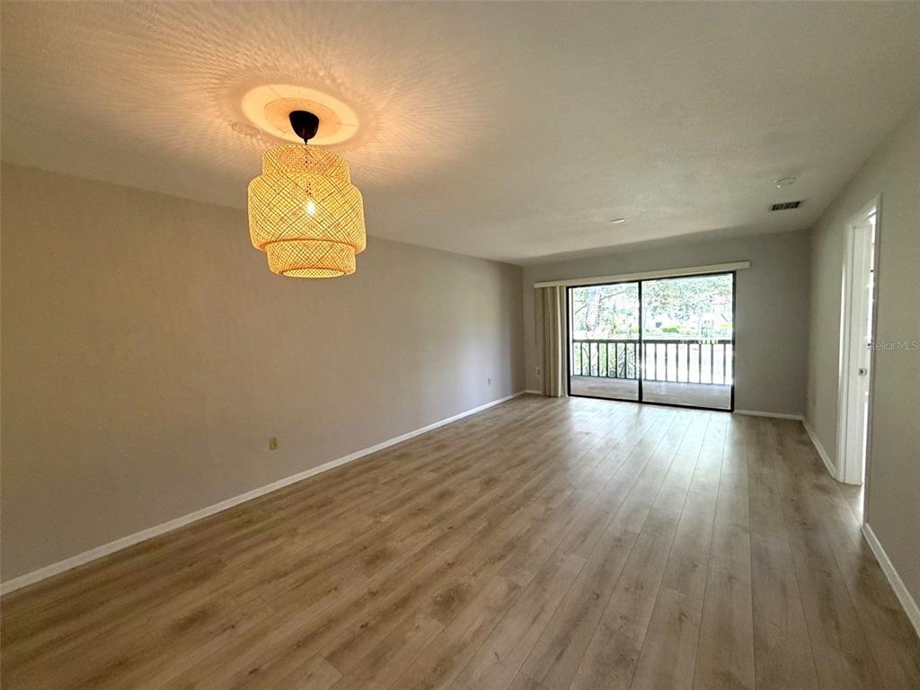 An empty living room features light wood-look flooring, neutral walls, and a woven pendant light — 5216 WILLOW LINKS UNIT 82, SARASOTA, FL