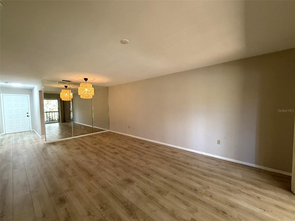 An empty living room features light wood-look flooring, beige walls, and a large mirrored wall — 5216 WILLOW LINKS UNIT 82, SARASOTA, FL