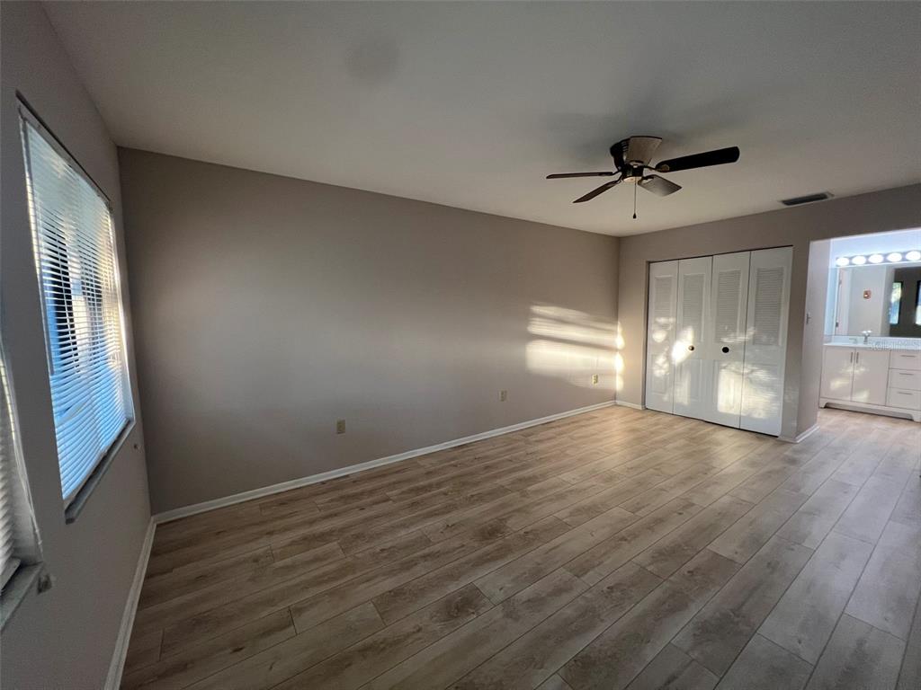 A bedroom with light-colored walls, wood-look flooring, a ceiling fan, and white closet doors — 5216 WILLOW LINKS UNIT 82, SARASOTA, FL