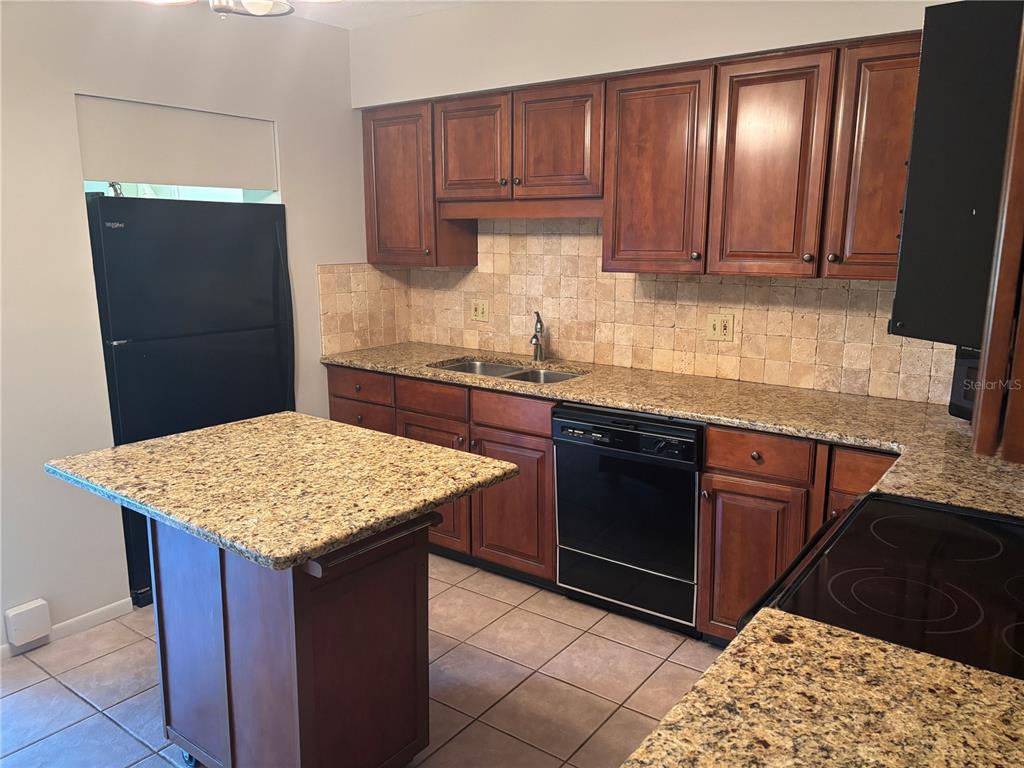 A kitchen features dark wood cabinets, granite countertops, a mobile island, and black appliances — 6645 1ST AVENUE N UNIT 307, ST PETERSBURG, FL