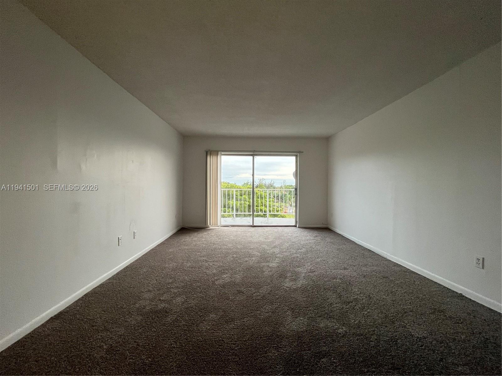 An empty room with dark carpeting, white walls, and a sliding glass door to a balcony — 492 NW 165th St Rd # 611, Miami FL 33169, MIAMI, FL