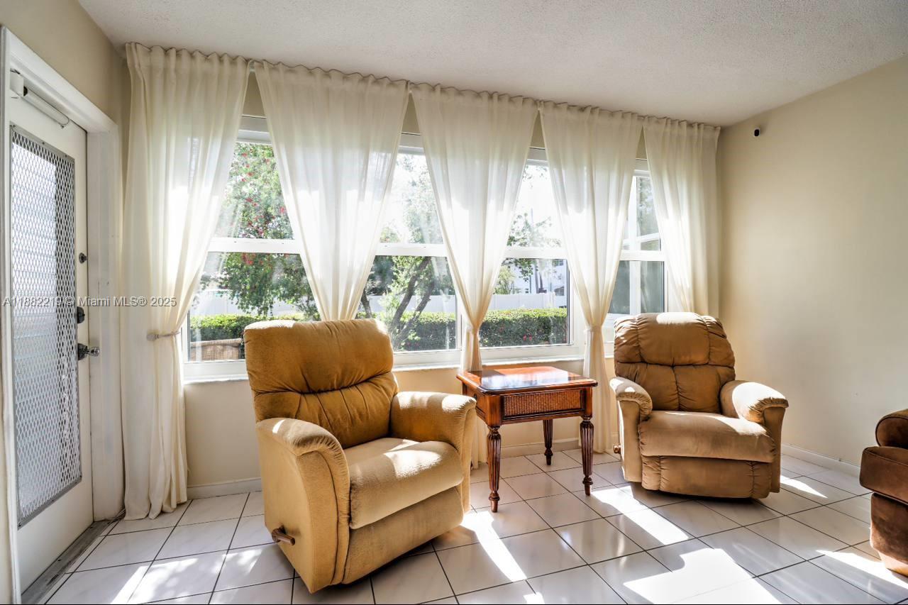 A sunroom features two tan recliners, a small wooden side table, and white tile flooring — 850 NE 12th Ave # 210, Hallandale Beach FL 33009, HALLANDALE BEACH, FL