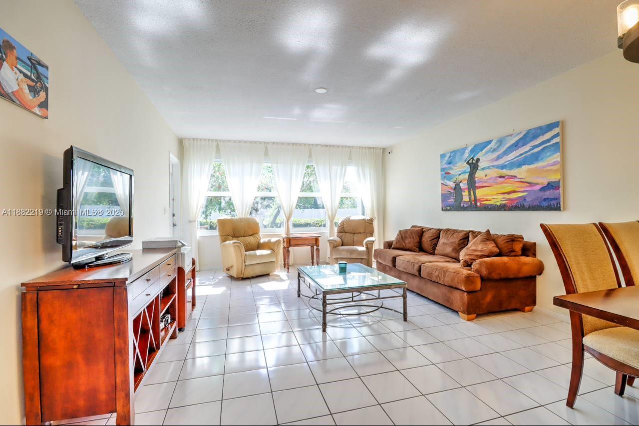 A living room features white tile floors, a brown sofa, two armchairs, and a television — 850 NE 12th Ave # 210, Hallandale Beach FL 33009, HALLANDALE BEACH, FL