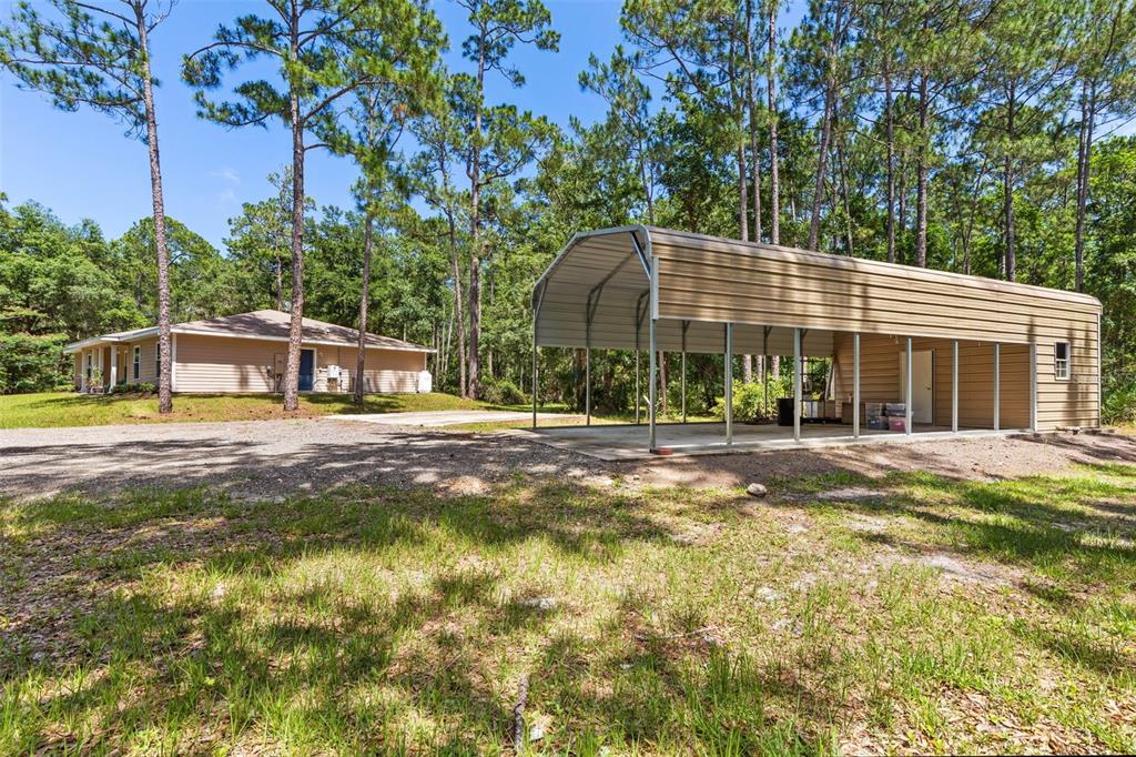 A tan house and a large metal carport sit on a gravel lot among trees — 3296 N OLD DIXIE HIGHWAY, BUNNELL, FL