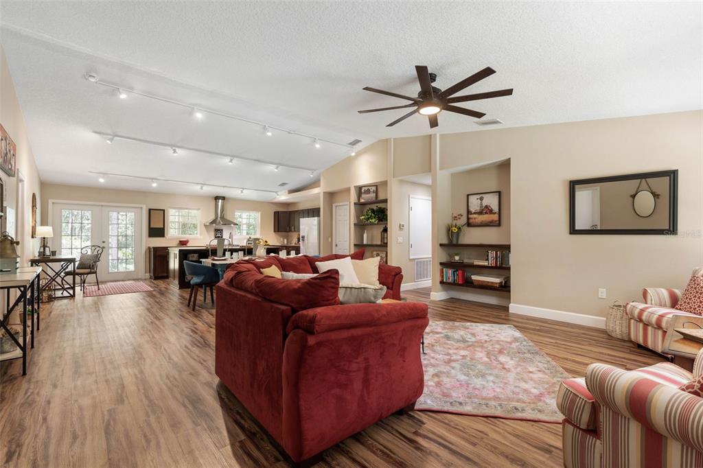 A spacious open-concept living room features wood-look flooring, a red sofa, and a vaulted ceiling — 3296 N OLD DIXIE HIGHWAY, BUNNELL, FL