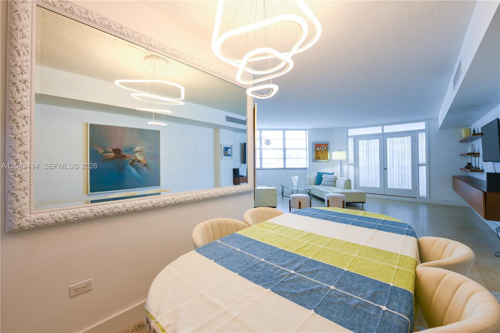 A dining area with a large mirror and modern light fixture opens into a living room — 801 Brickell Bay Dr # 1462, Miami FL 33131, MIAMI, FL