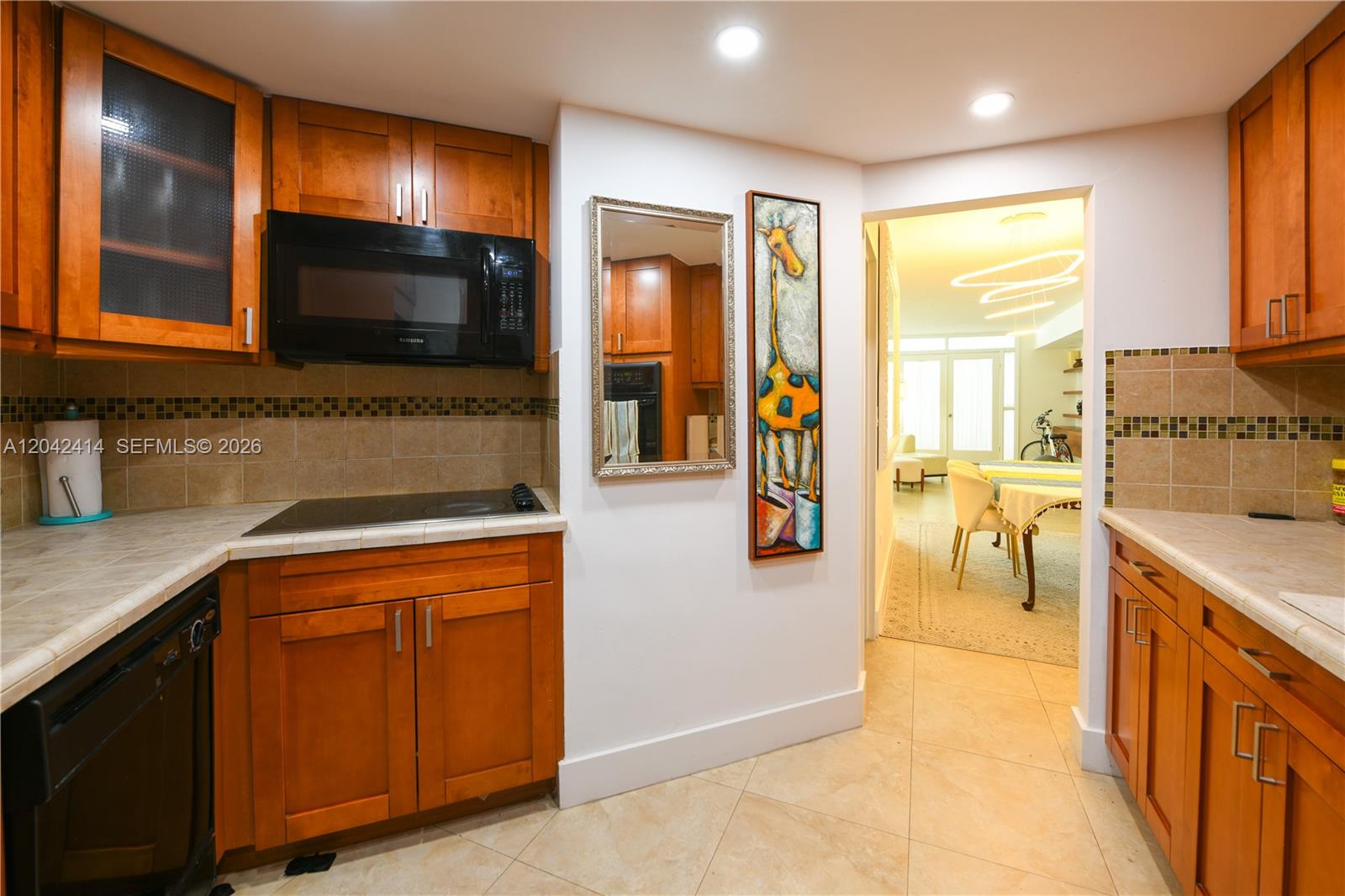 A kitchen features wooden cabinets, a black microwave, tiled countertops, and a giraffe wall art — 801 Brickell Bay Dr # 1462, Miami FL 33131, MIAMI, FL