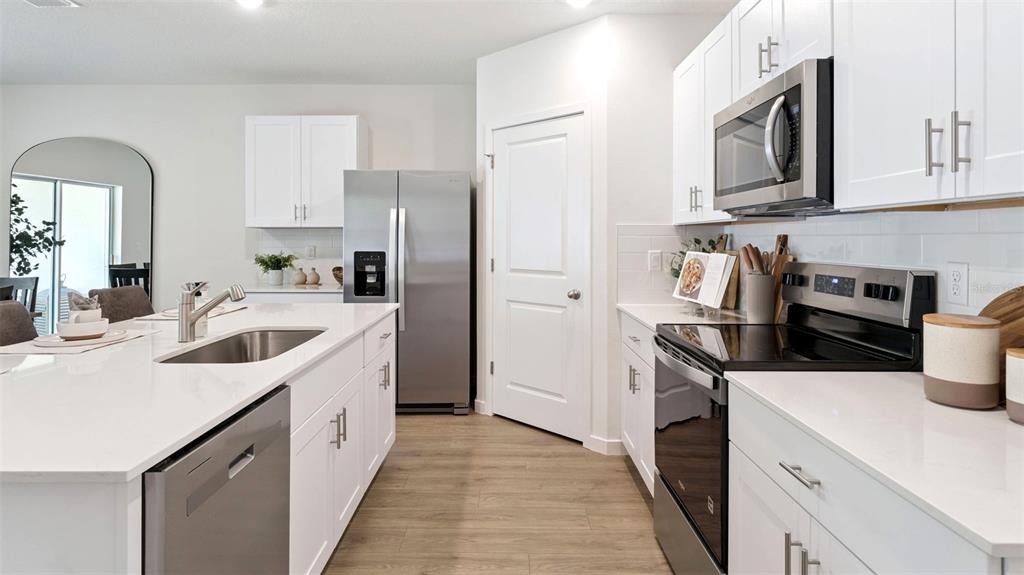 A modern kitchen features white cabinets, stainless steel appliances, and a large quartz-topped island — 1539 BEECHMONT DRIVE, KISSIMMEE, FL