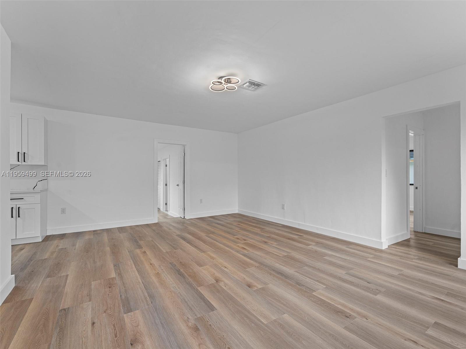A bright, empty room features white walls, wood-look flooring, and a modern ceiling light — 14545 Garden Dr, Miami FL 33168, MIAMI, FL