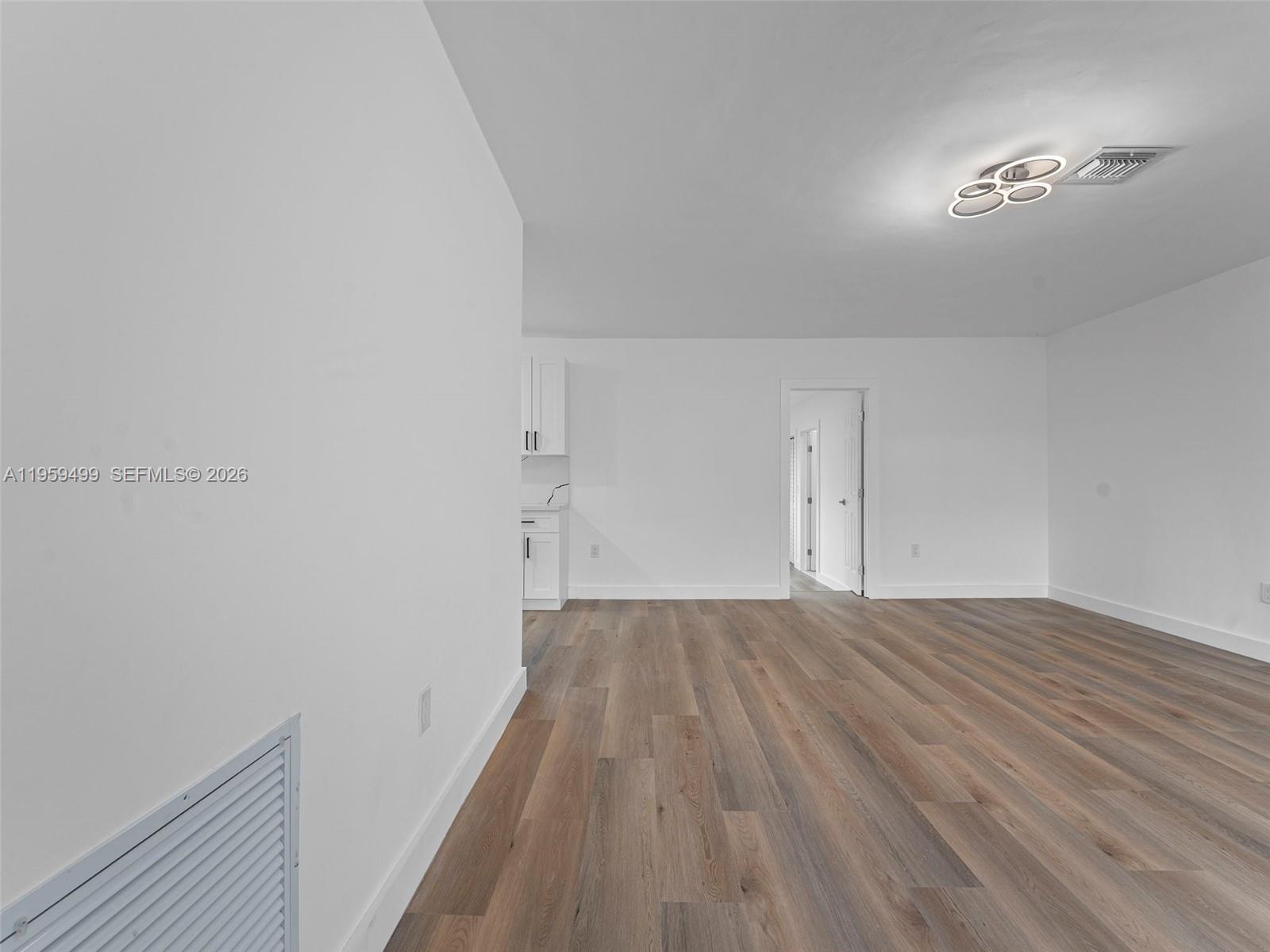 A bright, empty room features white walls, wood-look flooring, and a modern ceiling light fixture — 14545 Garden Dr, Miami FL 33168, MIAMI, FL