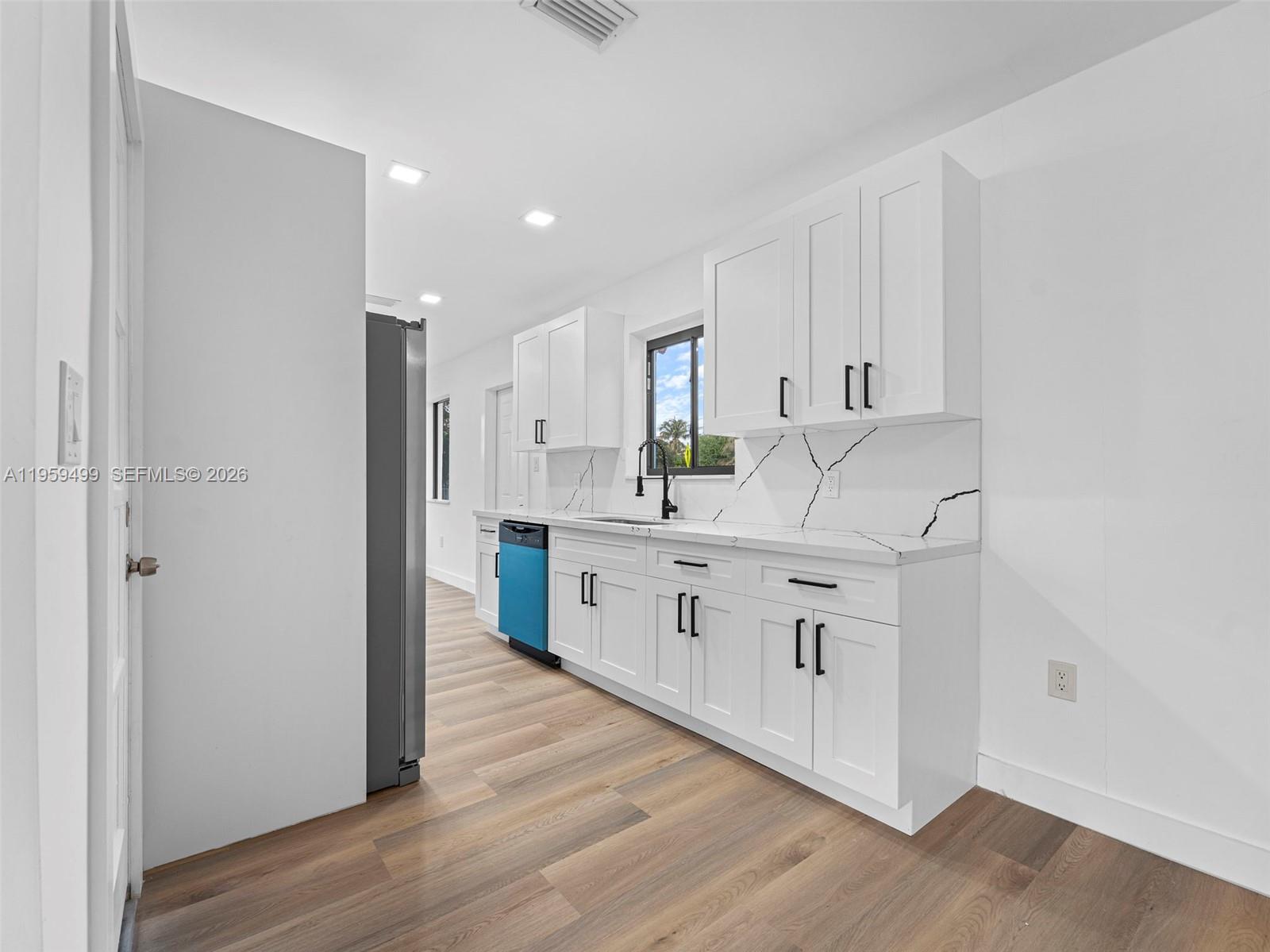 A kitchen features white cabinets, marble-patterned countertops, a blue dishwasher, and light wood flooring — 14545 Garden Dr, Miami FL 33168, MIAMI, FL