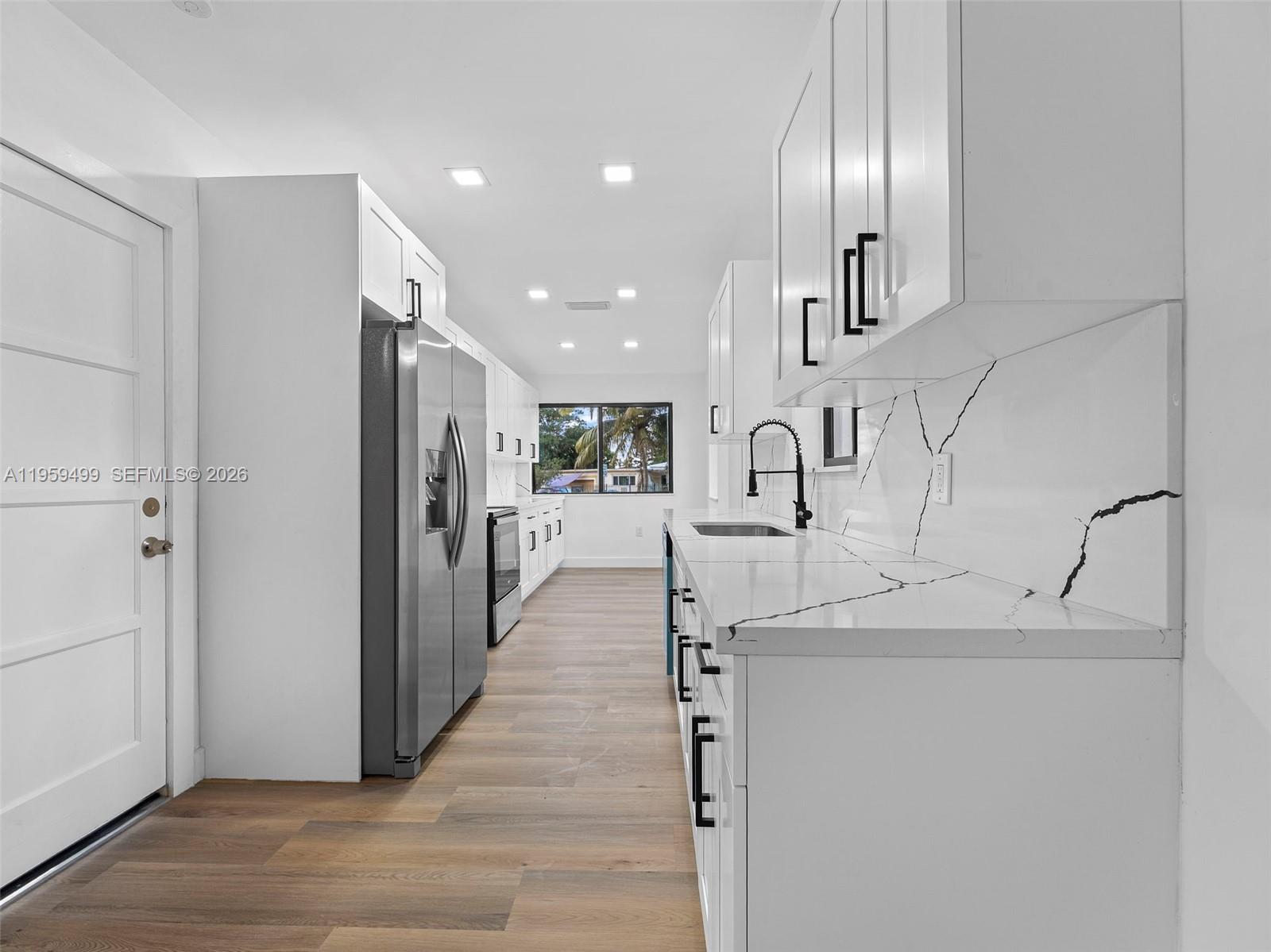 A modern kitchen features white cabinets, marble-patterned countertops, stainless steel appliances, and wood-look flooring — 14545 Garden Dr, Miami FL 33168, MIAMI, FL