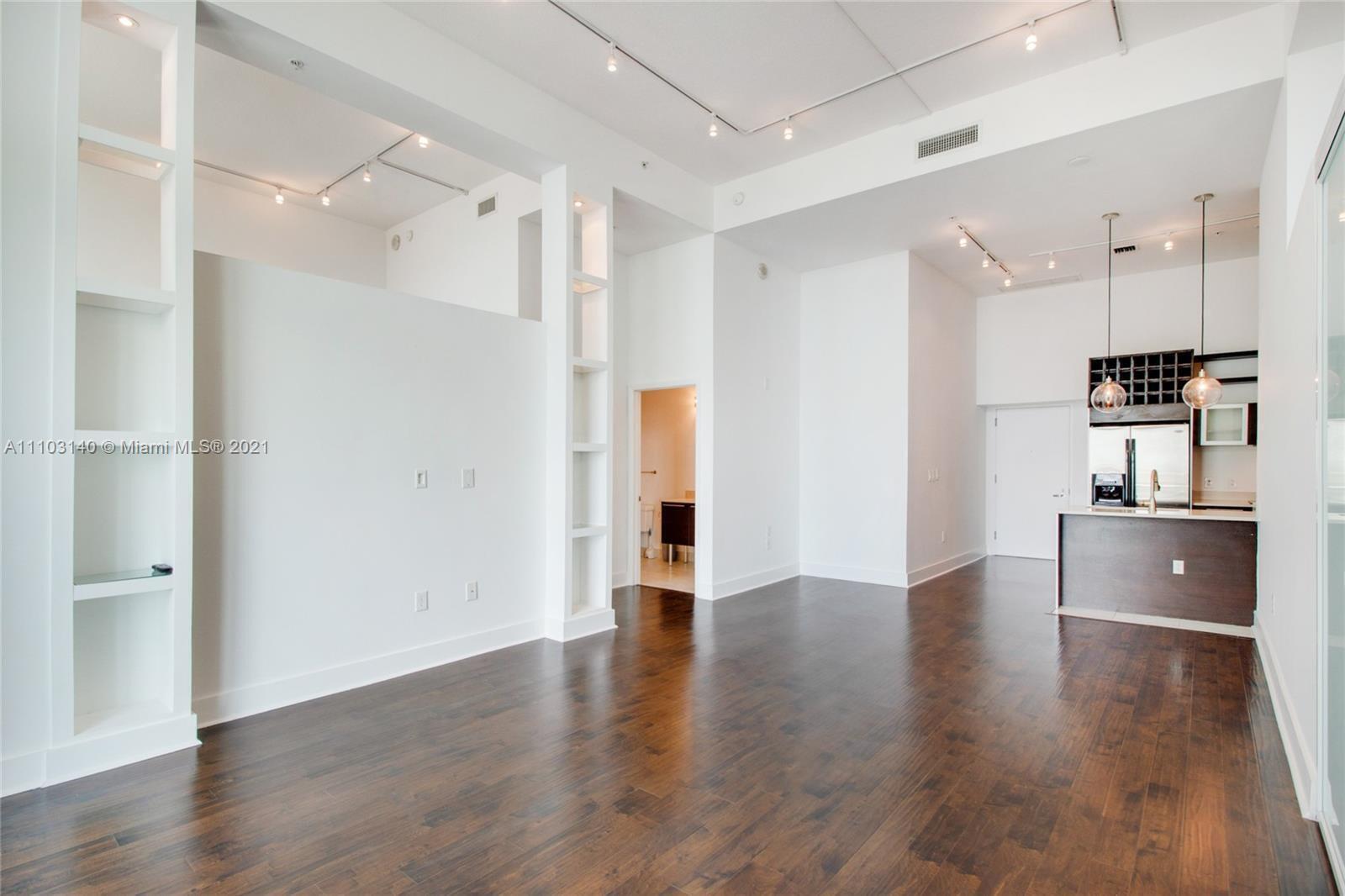 An open-concept living area features dark hardwood floors, white walls, and a small kitchen — 1900 N Bayshore Drive # 912, Miami FL 33132, MIAMI, FL