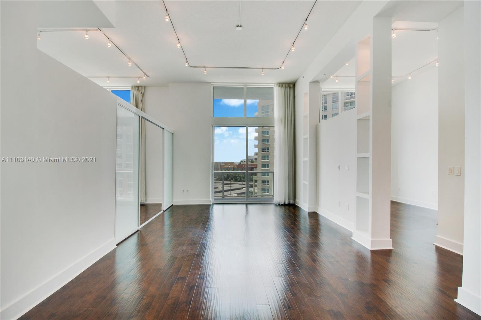 A bright, empty living area features dark hardwood floors, track lighting, and floor-to-ceiling windows — 1900 N Bayshore Drive # 912, Miami FL 33132, MIAMI, FL
