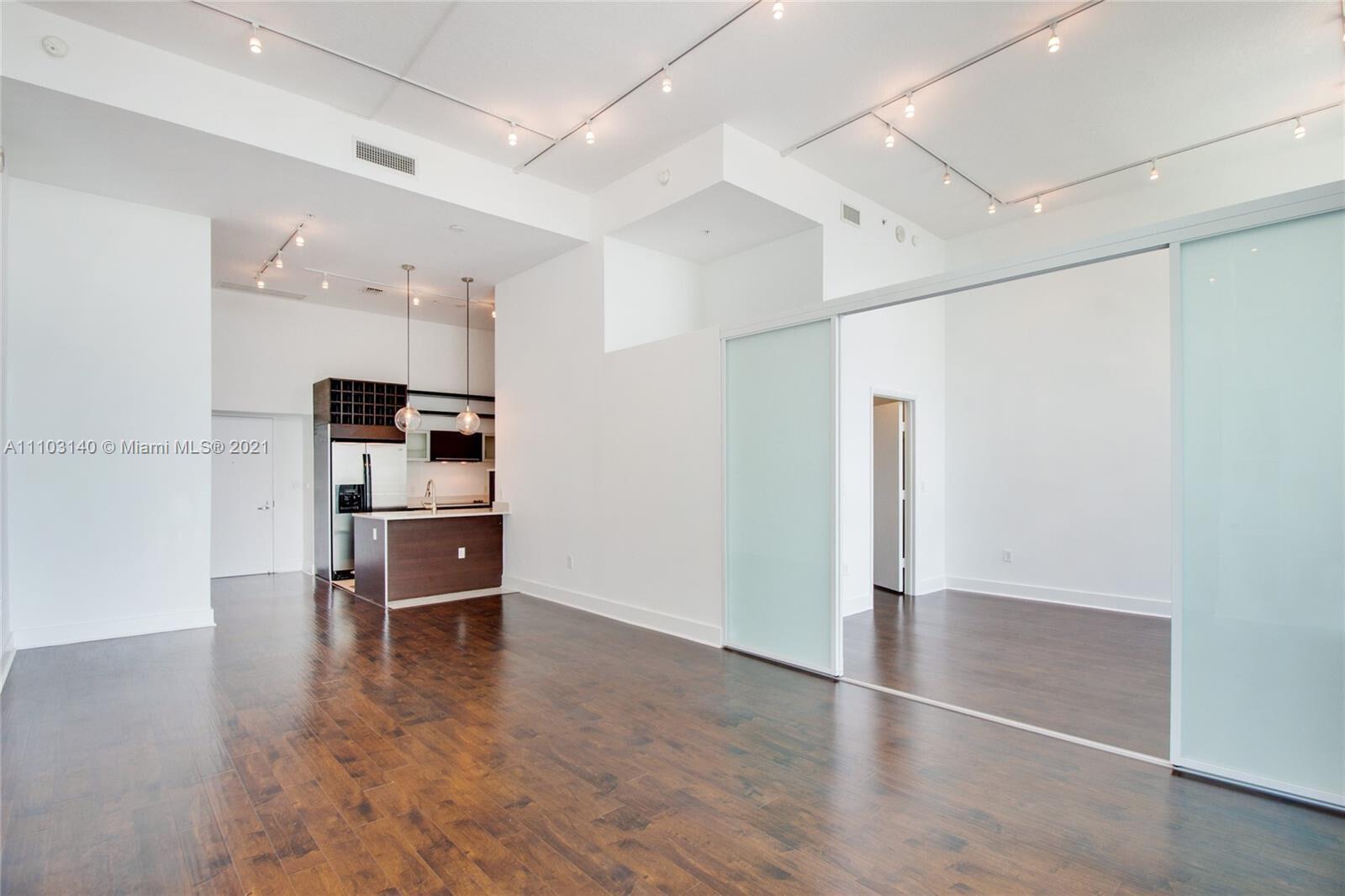 A modern open-concept living area features dark wood floors, white walls, and sliding glass doors — 1900 N Bayshore Drive # 912, Miami FL 33132, MIAMI, FL