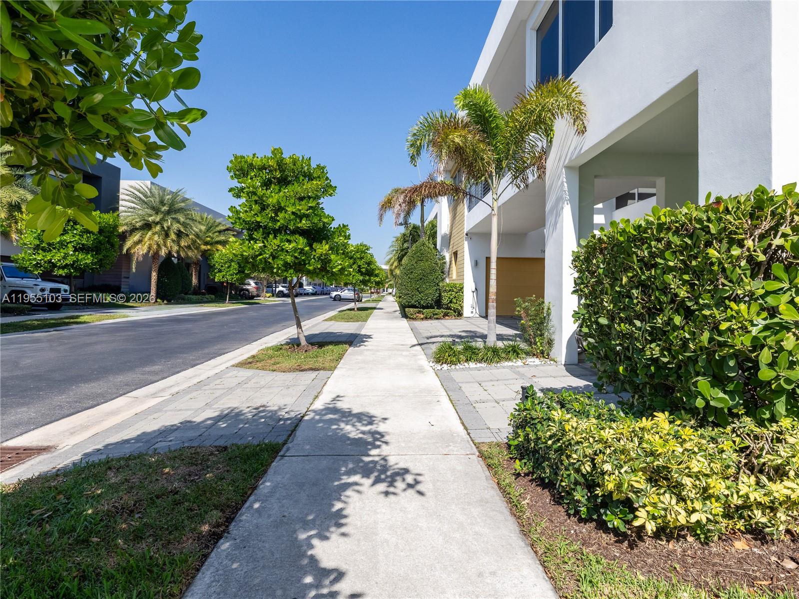A paved sidewalk runs alongside a modern white building with palm trees and landscaping — 7451 NW 103rd Ct, Doral FL 33178, DORAL, FL