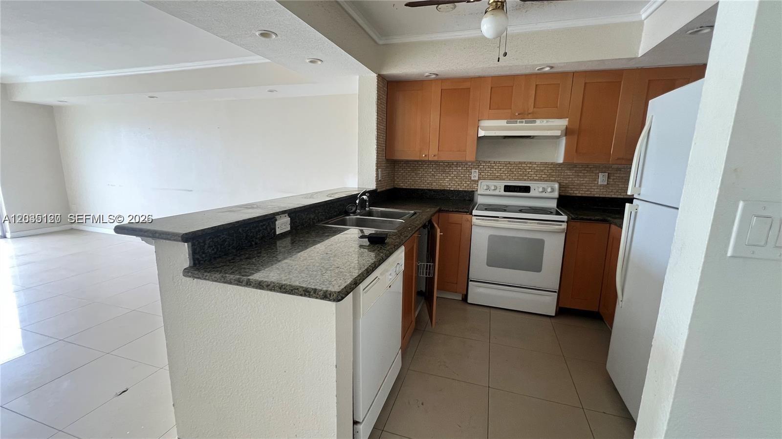 A kitchen features wooden cabinets, granite countertops, white appliances, and a breakfast bar — 486 NW 165th St Rd # 606, Miami FL 33169, MIAMI, FL