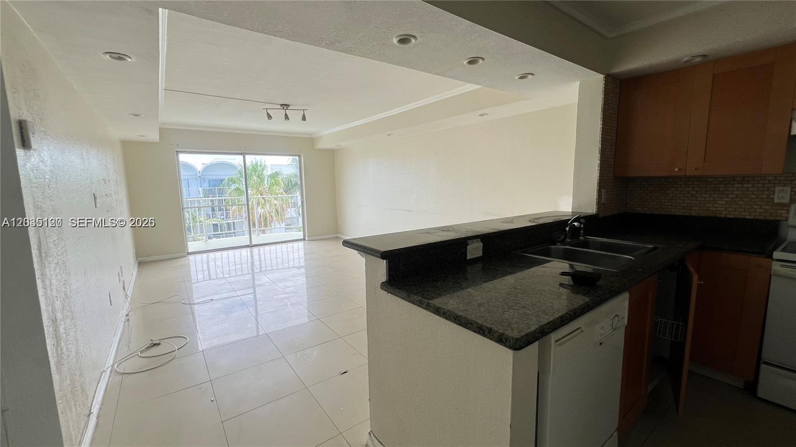 A kitchen with granite countertops overlooks a tiled living area with a sliding glass door — 486 NW 165th St Rd # 606, Miami FL 33169, MIAMI, FL
