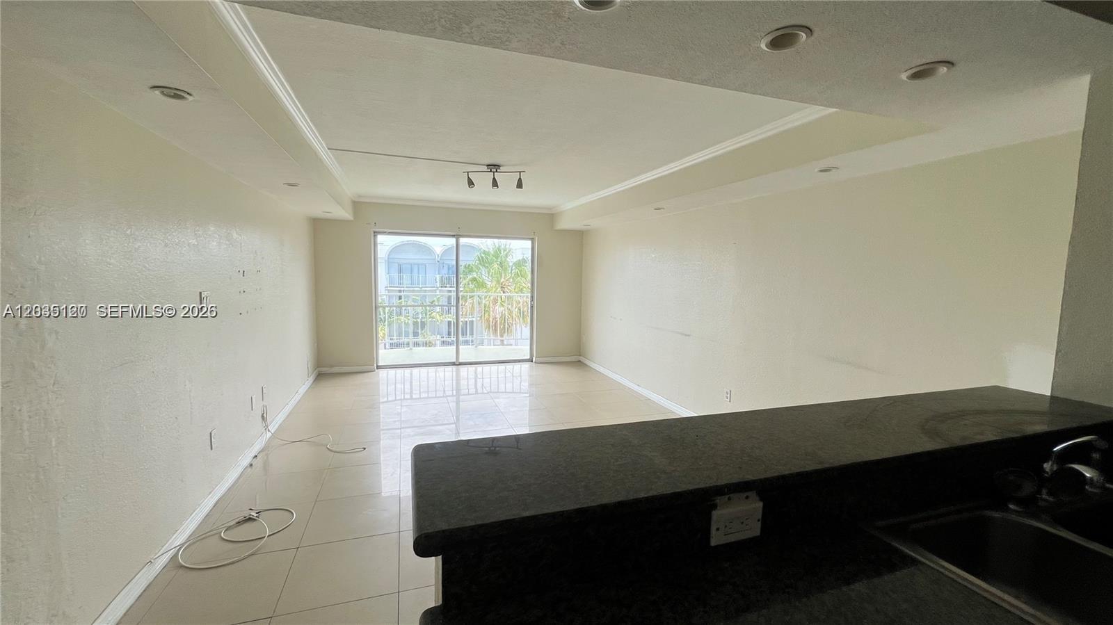 An empty living room features light tile floors, recessed lighting, and a sliding glass door — 486 NW 165th St Rd # 606, Miami FL 33169, MIAMI, FL