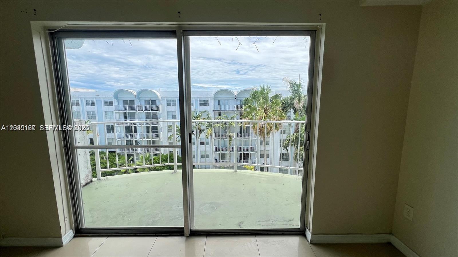 A sliding glass door opens onto a balcony overlooking a neighboring apartment building — 486 NW 165th St Rd # 606, Miami FL 33169, MIAMI, FL