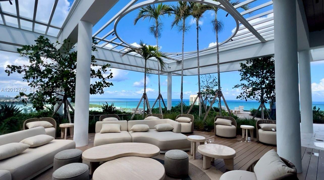 An outdoor lounge area features modern beige furniture under a circular pergola overlooking the ocean — 580 72nd St # 1111, Miami Beach FL 33141, MIAMI BEACH, FL