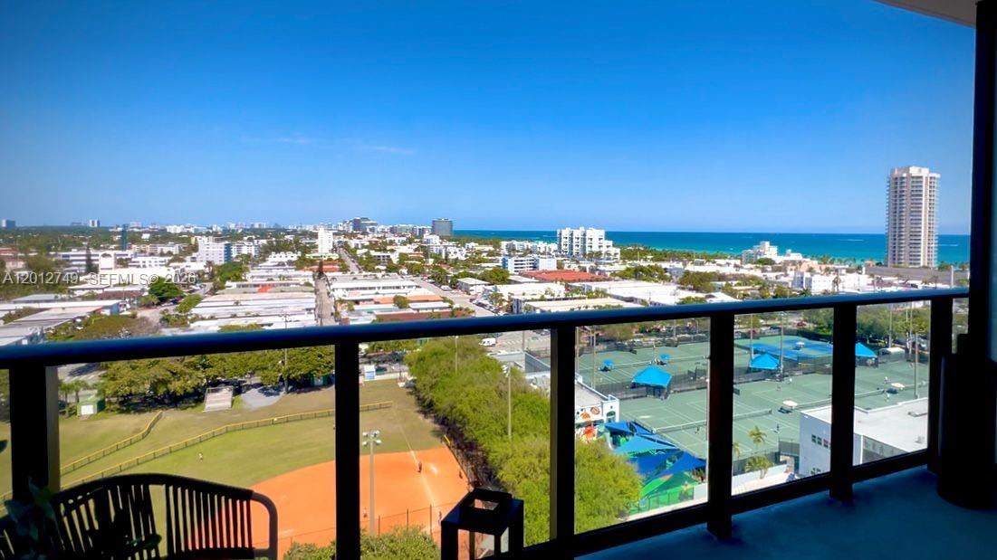 A high-rise balcony view overlooks a baseball field, tennis courts, city buildings, and the ocean — 580 72nd St # 1111, Miami Beach FL 33141, MIAMI BEACH, FL