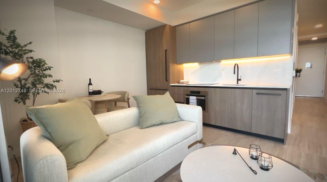 A modern studio apartment features a kitchen with grey cabinetry, a sofa, and a dining area — 580 72nd St # 1111, Miami Beach FL 33141, MIAMI BEACH, FL