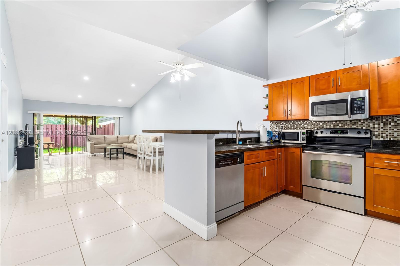 An open-concept kitchen with wood cabinets and stainless steel appliances overlooks a living area — 505 NE 199th Ln # 2A, Miami FL 33179, MIAMI, FL