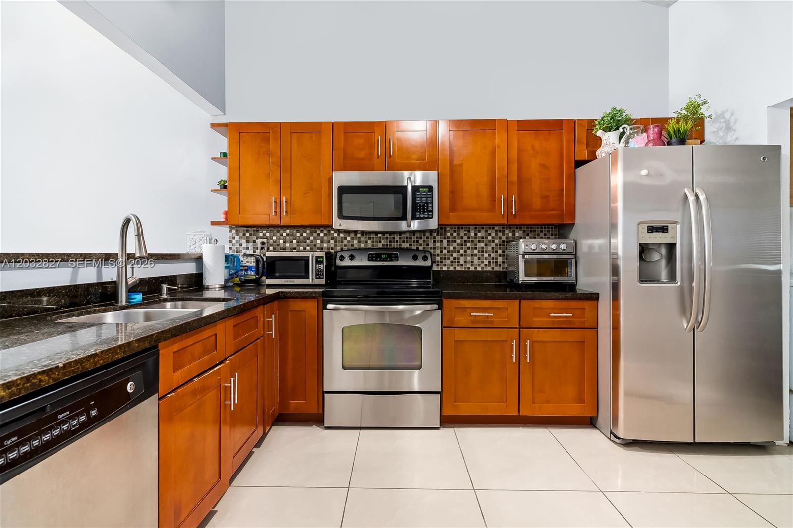 A kitchen features wood cabinets, stainless steel appliances, dark countertops, and light tile flooring — 505 NE 199th Ln # 2A, Miami FL 33179, MIAMI, FL