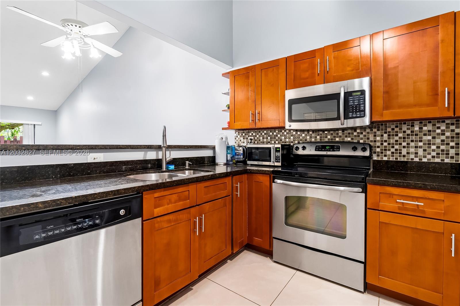 A kitchen features wood cabinets, stainless steel appliances, dark countertops, and a tiled backsplash — 505 NE 199th Ln # 2A, Miami FL 33179, MIAMI, FL