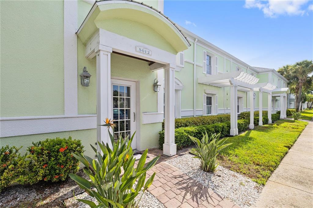 A light green building exterior features a covered entryway with white columns and a brick walkway — 5012 STARFISH DRIVE SE UNIT C, ST PETERSBURG, FL
