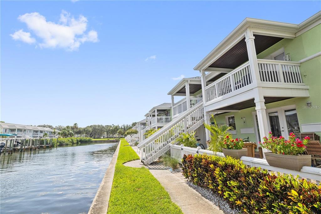 A row of light green waterfront townhomes features white balconies, exterior stairs, and landscaped patios — 5012 STARFISH DRIVE SE UNIT C, ST PETERSBURG, FL