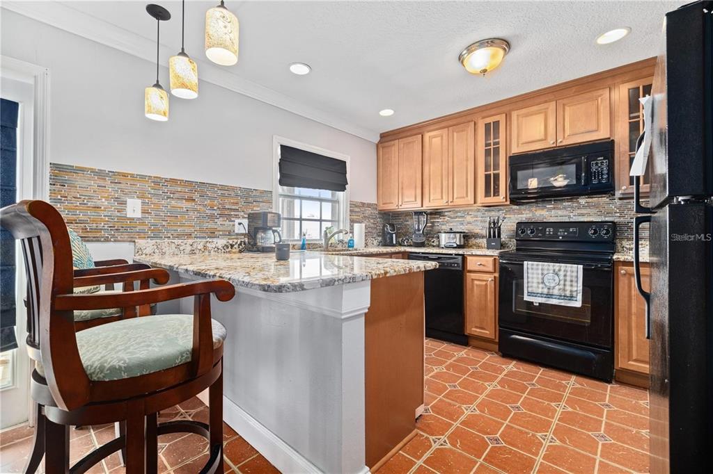 A kitchen with light wood cabinets, granite countertops, a black stove, and tiled flooring — 5012 STARFISH DRIVE SE UNIT C, ST PETERSBURG, FL