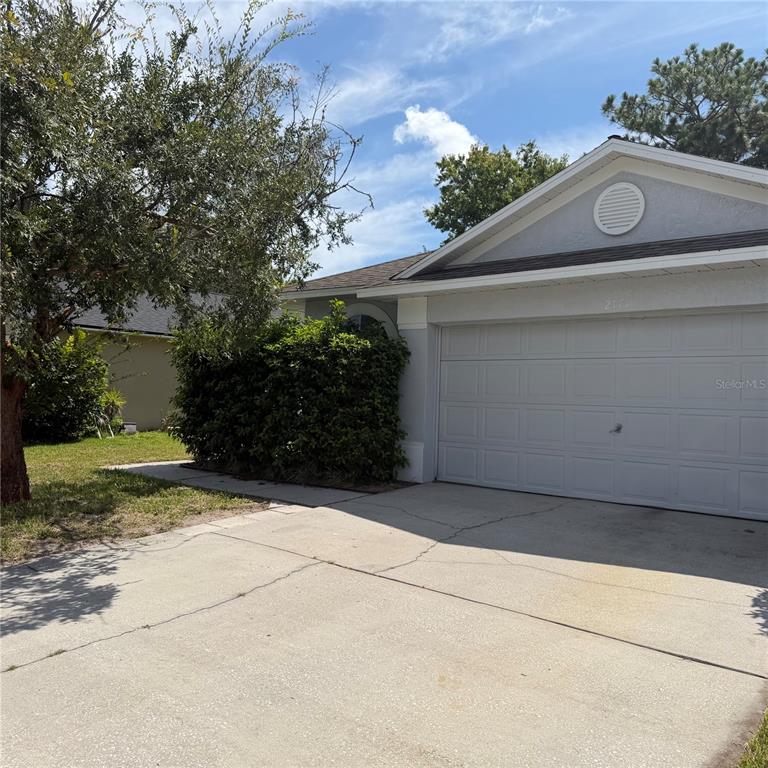 A single-story house exterior features a gray garage, a concrete driveway, and a large bush — 2171 EOLA COURT, OVIEDO, FL