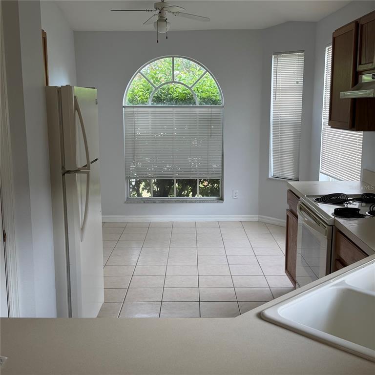 A kitchen with tile flooring, white appliances, wooden cabinets, and a large arched window — 2171 EOLA COURT, OVIEDO, FL