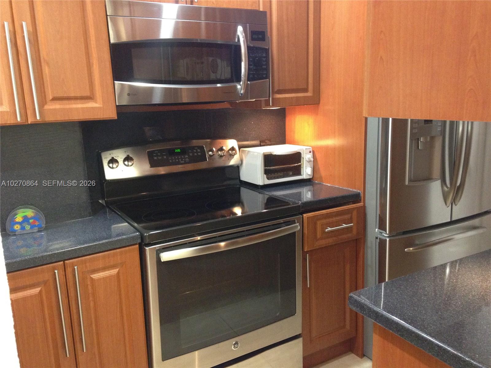A kitchen features wood cabinets, stainless steel appliances, and dark countertops — 3505 S Ocean Dr # 104, Hollywood FL 33019, HOLLYWOOD, FL