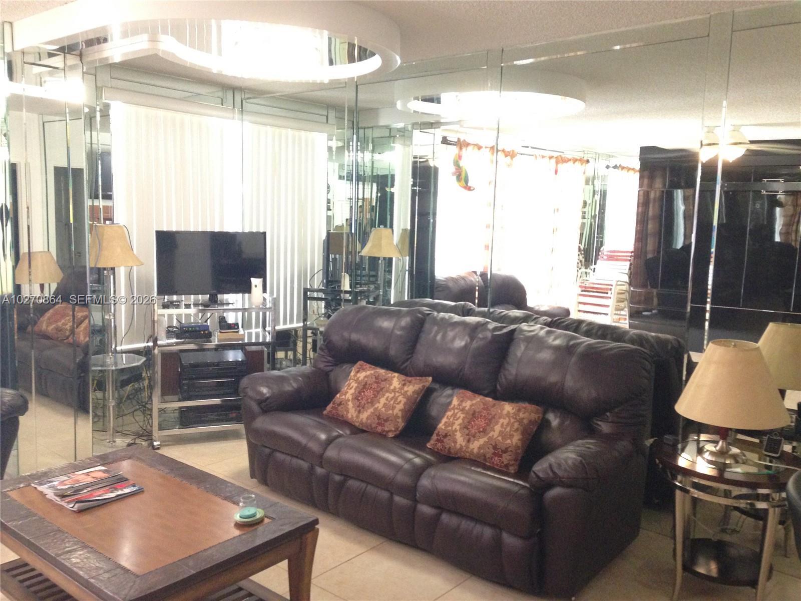 A living room features a dark leather sofa, a coffee table, and mirrored wall panels — 3505 S Ocean Dr # 104, Hollywood FL 33019, HOLLYWOOD, FL