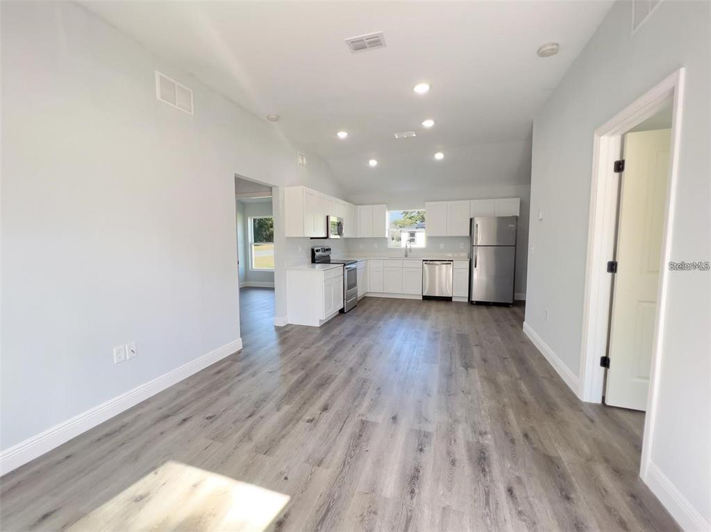 A bright kitchen with white cabinets, stainless steel appliances, and gray wood-look flooring — 3633 SE 138TH PLACE, SUMMERFIELD, FL