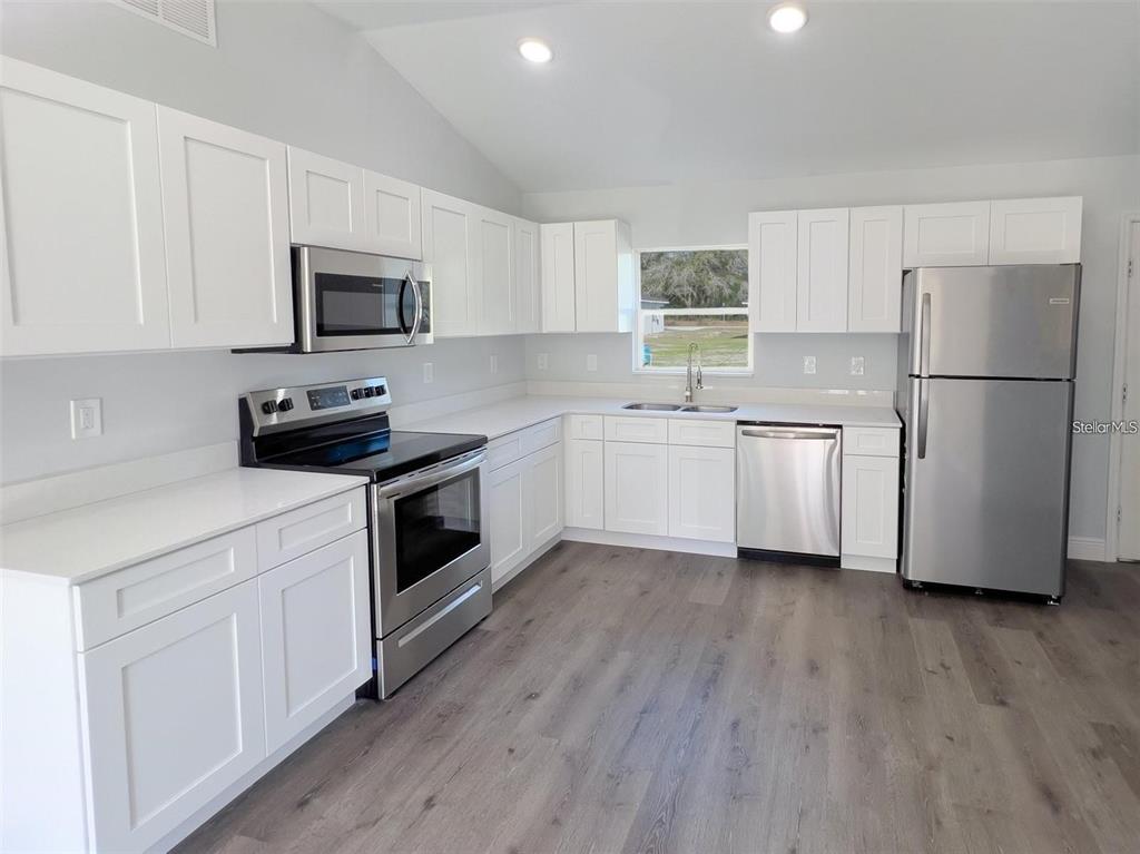 A kitchen with white cabinets, stainless steel appliances, white countertops, and wood-look flooring — 3633 SE 138TH PLACE, SUMMERFIELD, FL