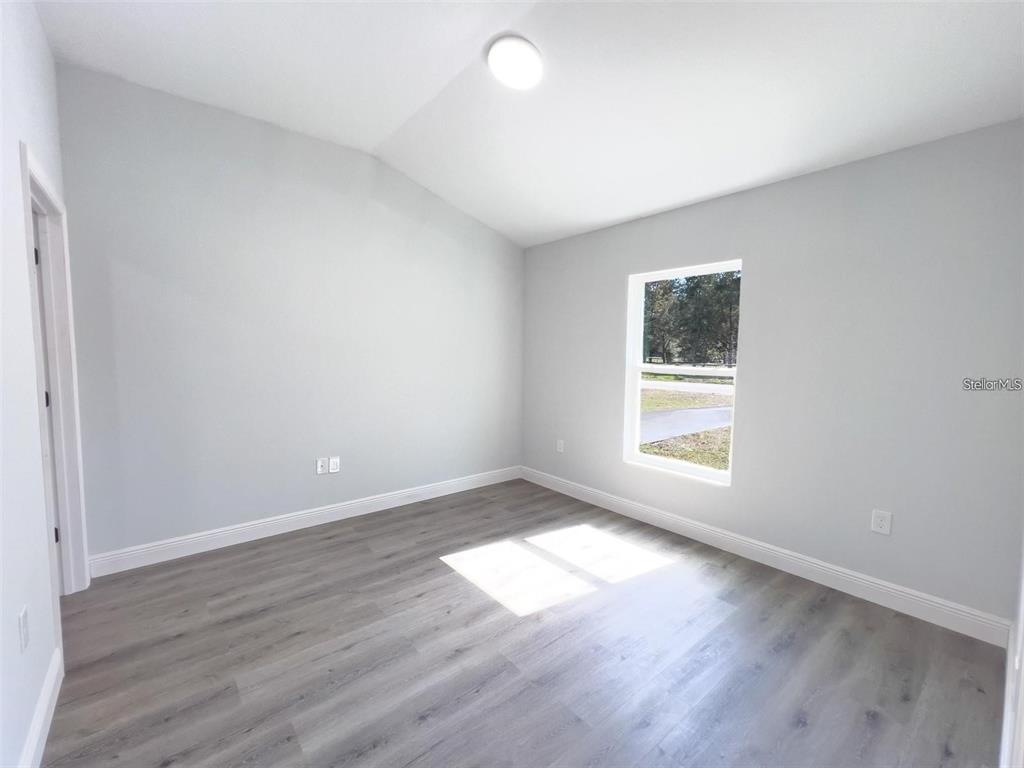 An empty room features light gray walls, wood-look flooring, a window, and a ceiling light — 3633 SE 138TH PLACE, SUMMERFIELD, FL
